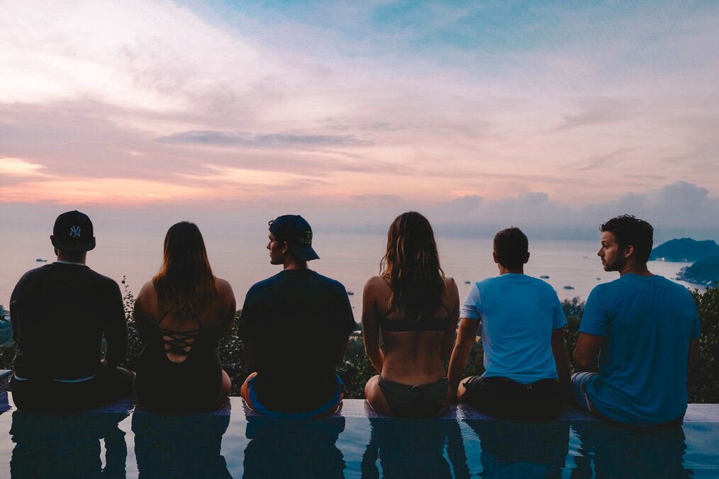 Study abroad students sitting at the edge of an infinity pool looking out at the pink an blue sunset together